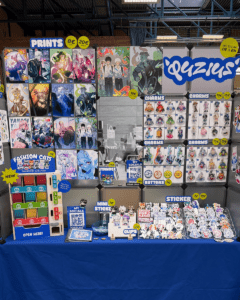 Messestand von Quzius mit Anime-Prints, Charms und Stickern unter blauem Schriftzug